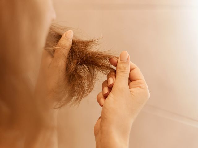 Manos de mujer sosteniendo un mechón de pelo dañado